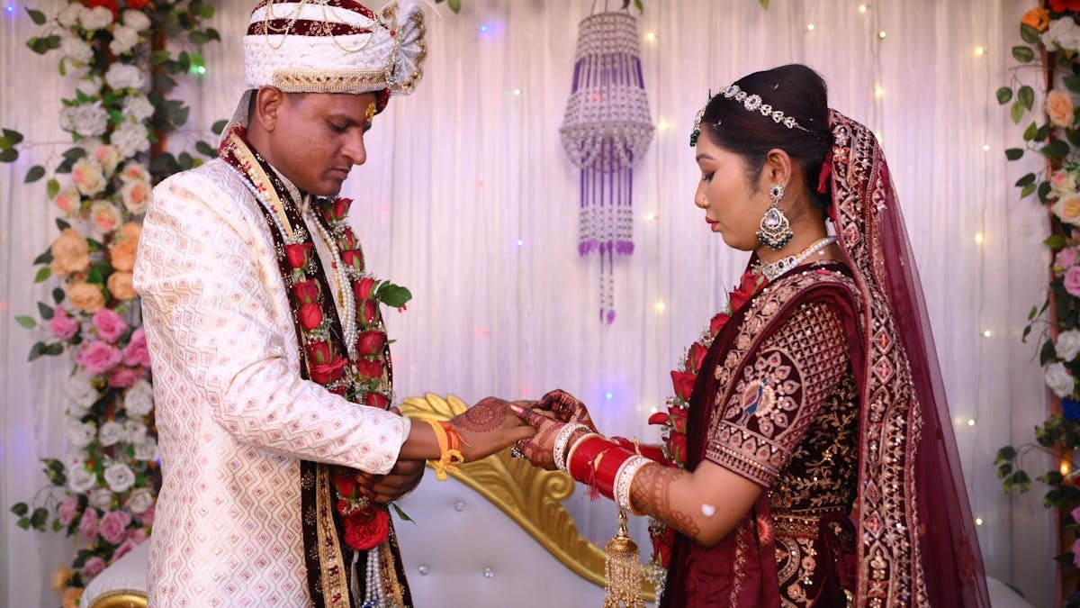 A couple exchanges rings in a traditional Indian wedding ceremony, adorned in vibrant attire with floral decorations.